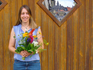 Frau steht mit Blumen in der Hand vor einer Holztür